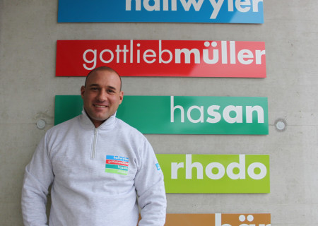 Neuer Mitarbeiter Maic von Felten steht stolz vor den fünf Hallwyler Gruppe Logos.